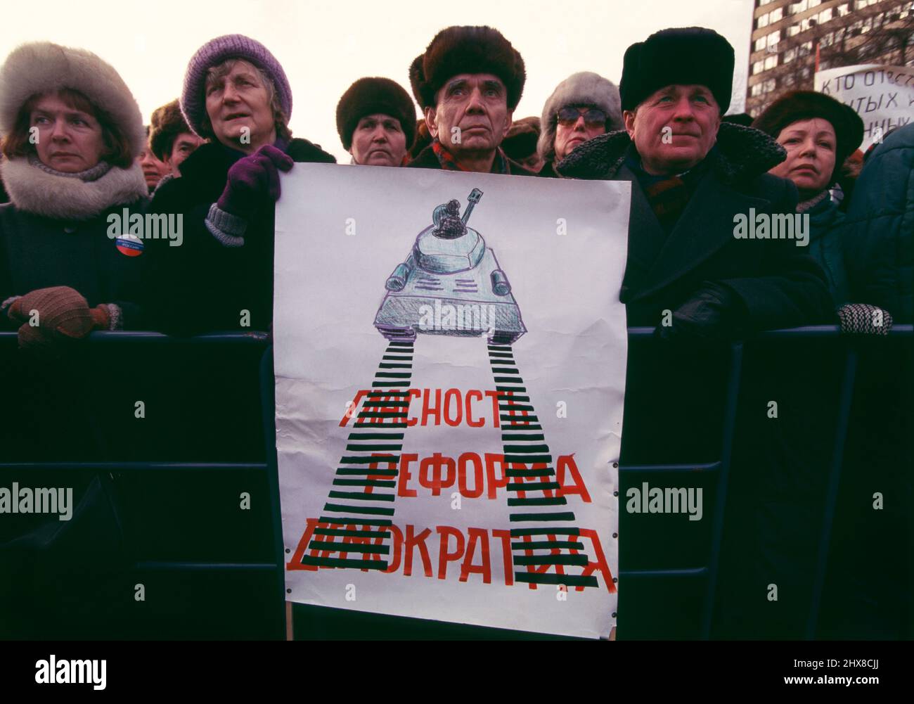 February 1995, Moscow, Russia.  Russians during an anti-war demonstration on Pushkin Square in central Moscow.  The demonstration was organized by Memorial and Soldiers’ Mothers in protest of the First Chechen War (1994-1996).   The protesters stand behind a poster showing a Russian tank driving over the words “Glasnost, Reform, Democracy” written in Cyrillic. Stock Photo