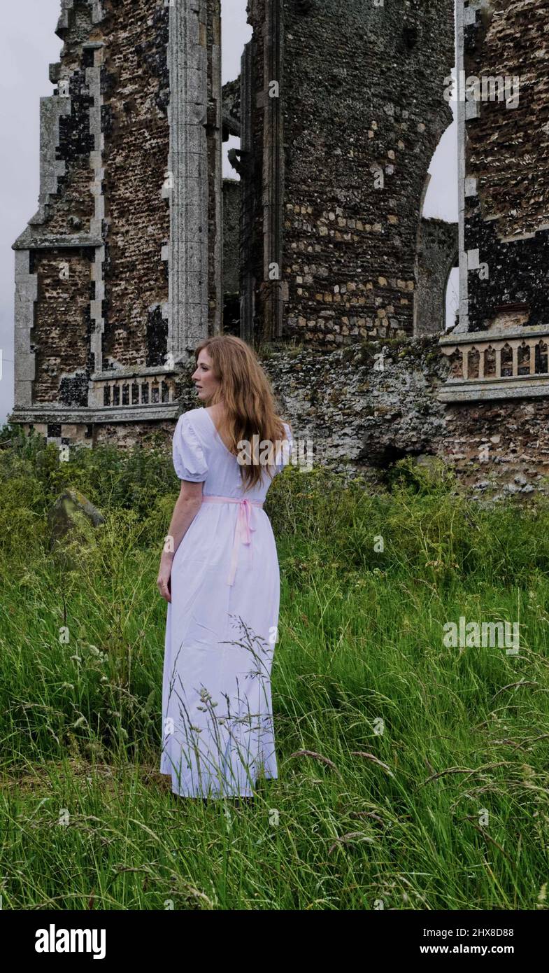 Ghostly pale young woman in white dress standing by the ruins of an old Norman church Stock Photo