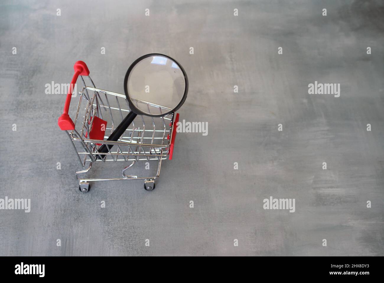 Magnifying glass inside shopping trolley. Product search and frugal shopping concept. Stock Photo