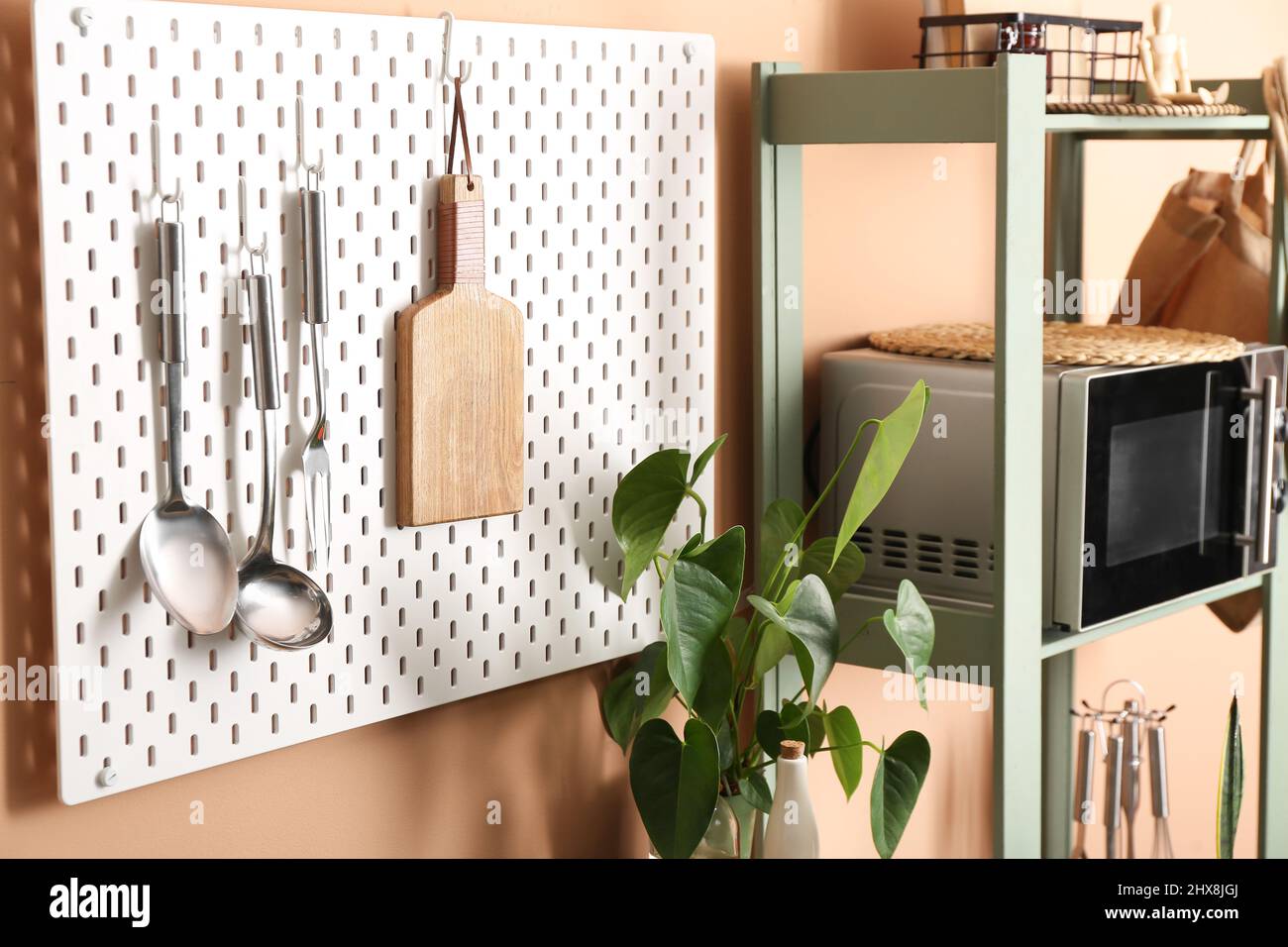Pegboard with kitchen utensils and shelf unit near color wall Stock