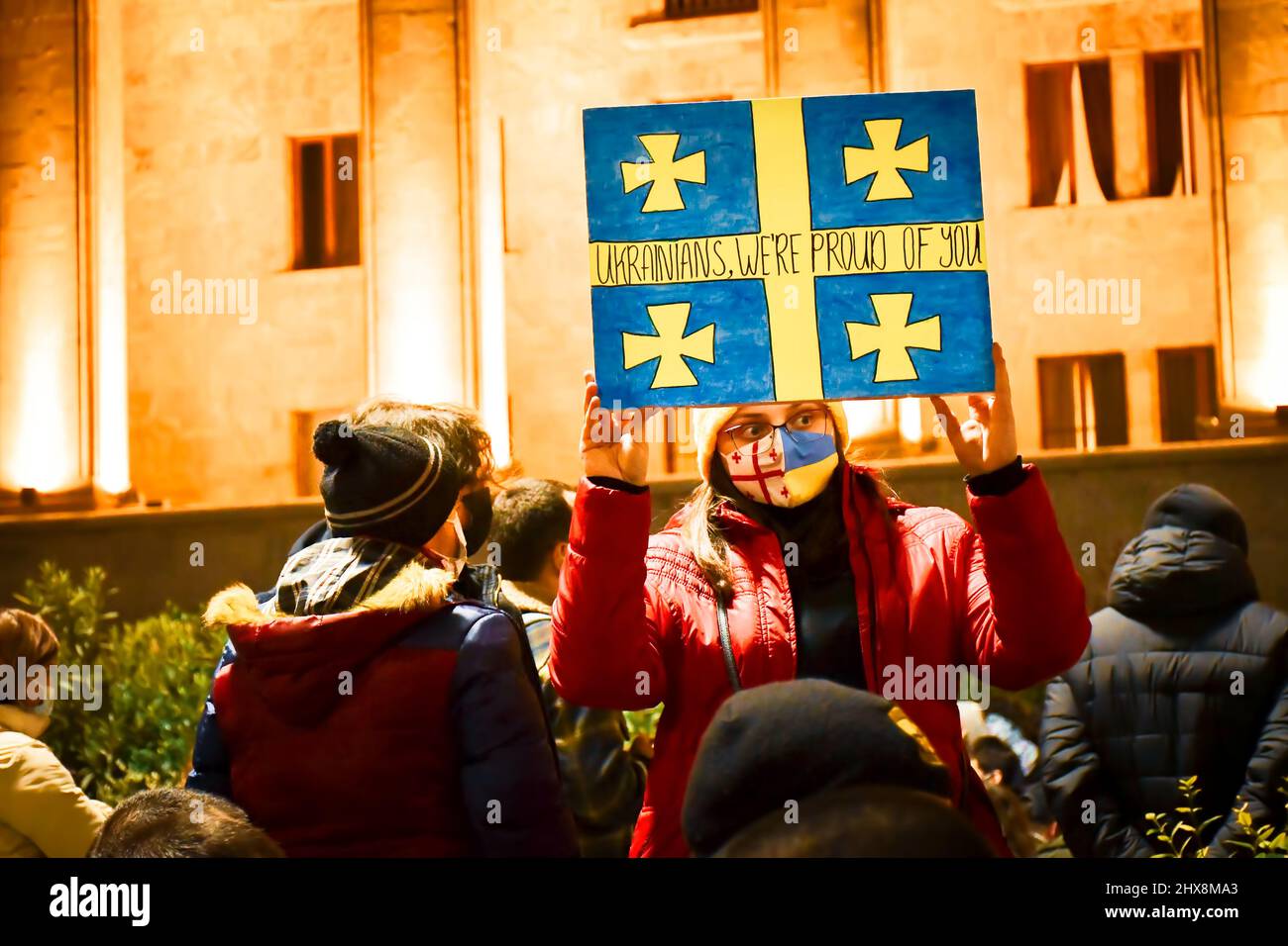 Tbilisi, Georgia - 1st march, 2022: woman with georgian ukrainian face mask hold and show hand- made painting of Ukrainian flag with title "Ukrainians Stock Photo