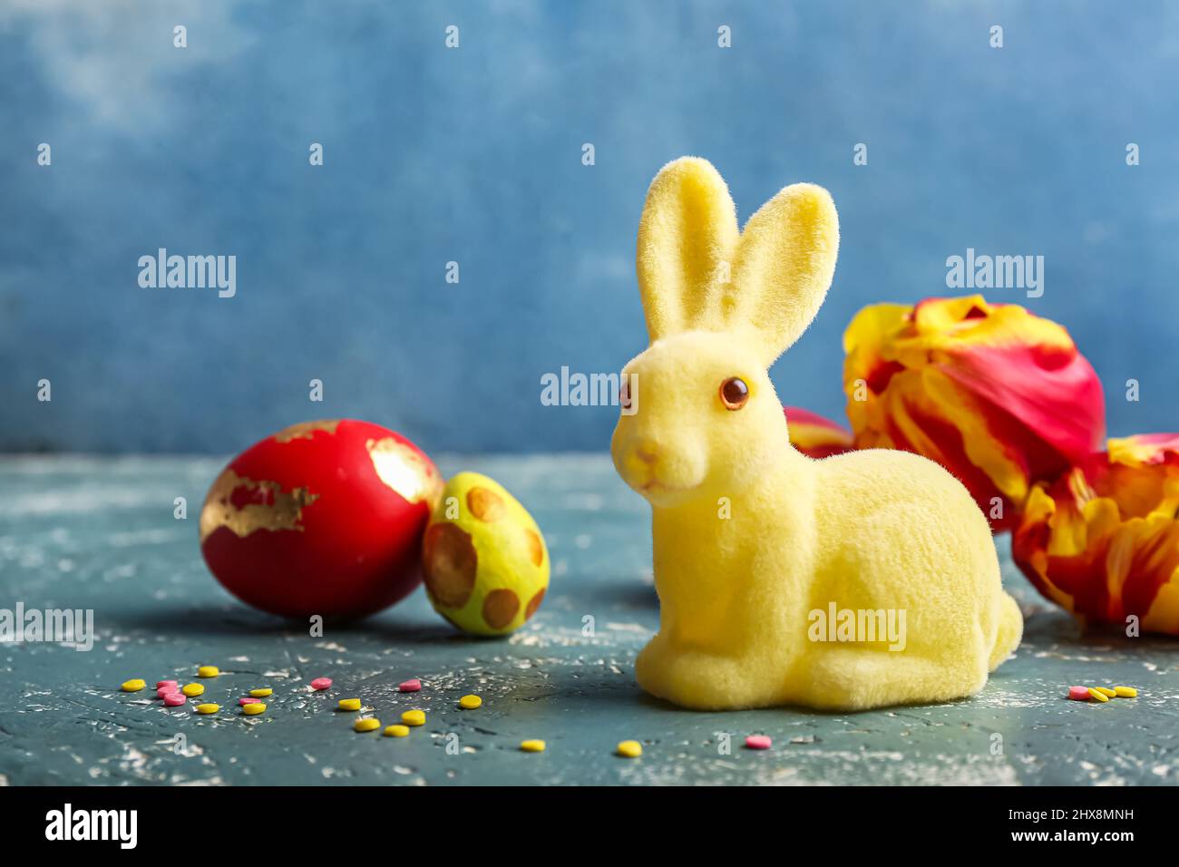 Cute Easter bunny with painted eggs and flowers on color background ...