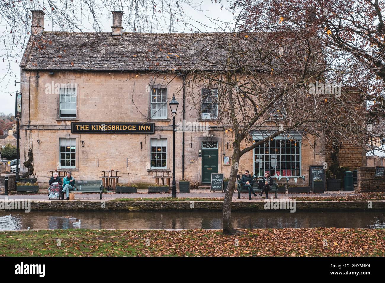 People take a pause on benches outside a traditional pub in this sleepy Cotswold town. Stock Photo