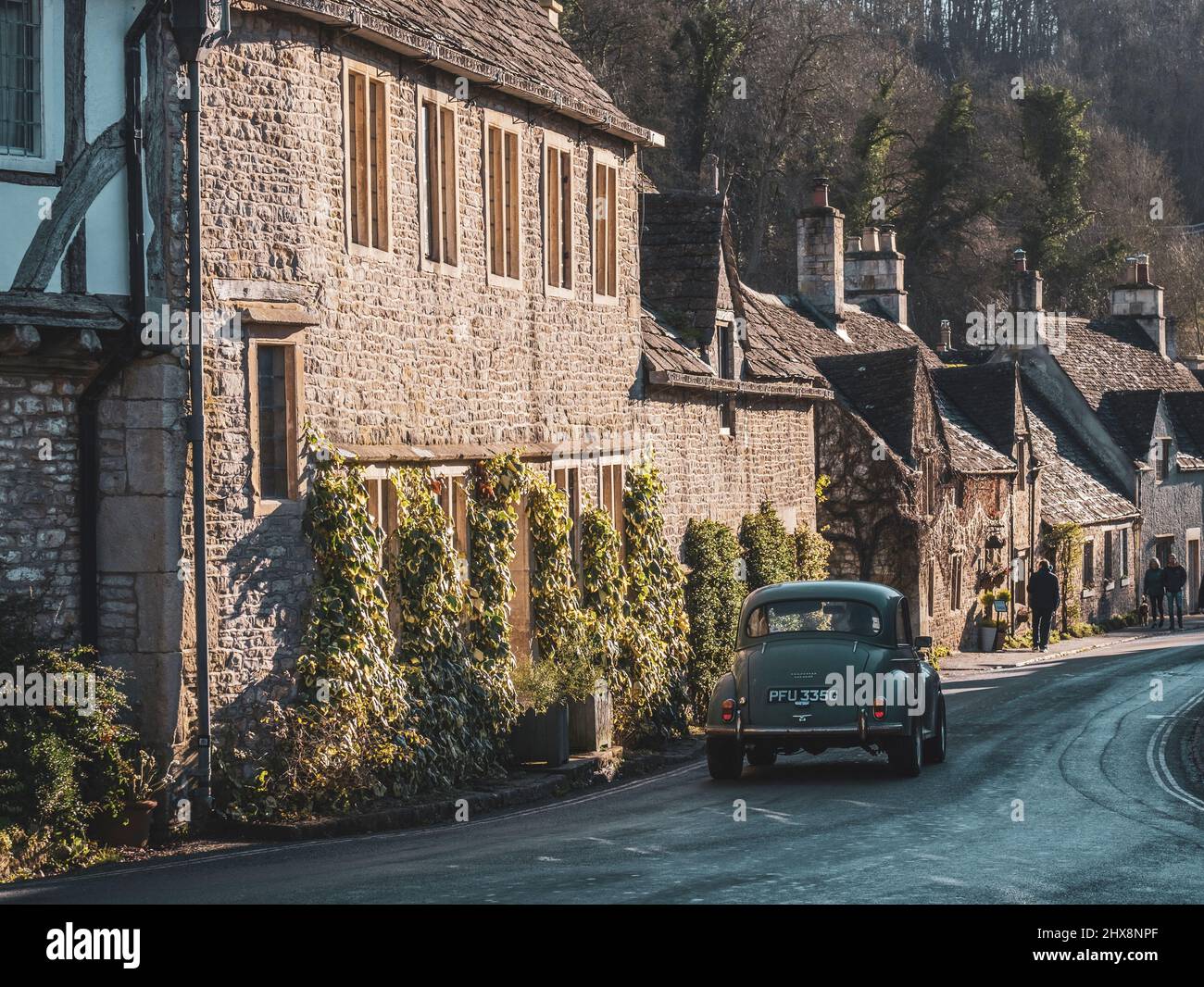 A green vintage car Minor 1000 drives through this quaint Cotswolds location. Stock Photo