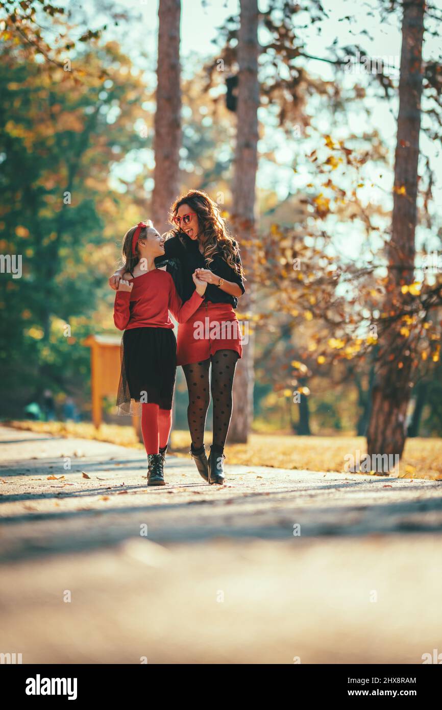 Beautiful young mother and her happy daughter are walking and having fun in the forest in sunset. They are holding hands and laughing. Stock Photo