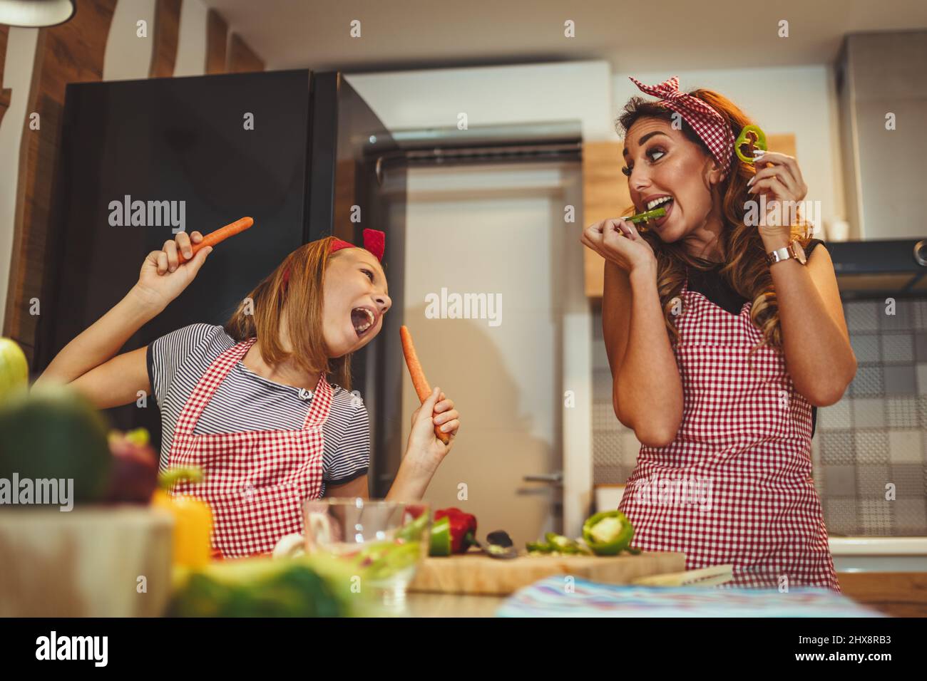 Happy mother and her daughter enjoy and having fun in making and having healthy meal together at their home kitchen. Stock Photo