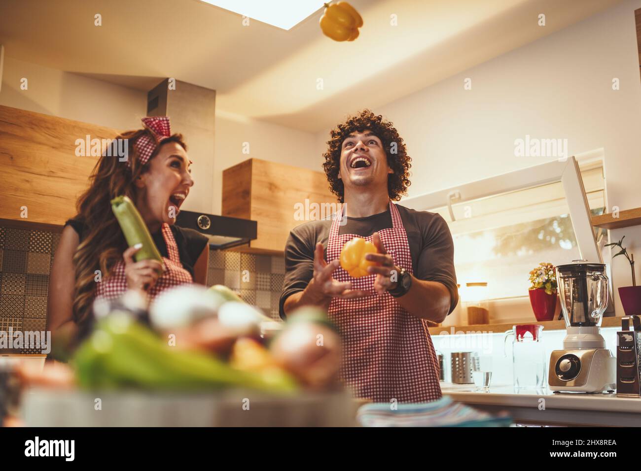 Happy young couple enjoys and having fun in making and having healthy meal together at their home kitchen. Stock Photo