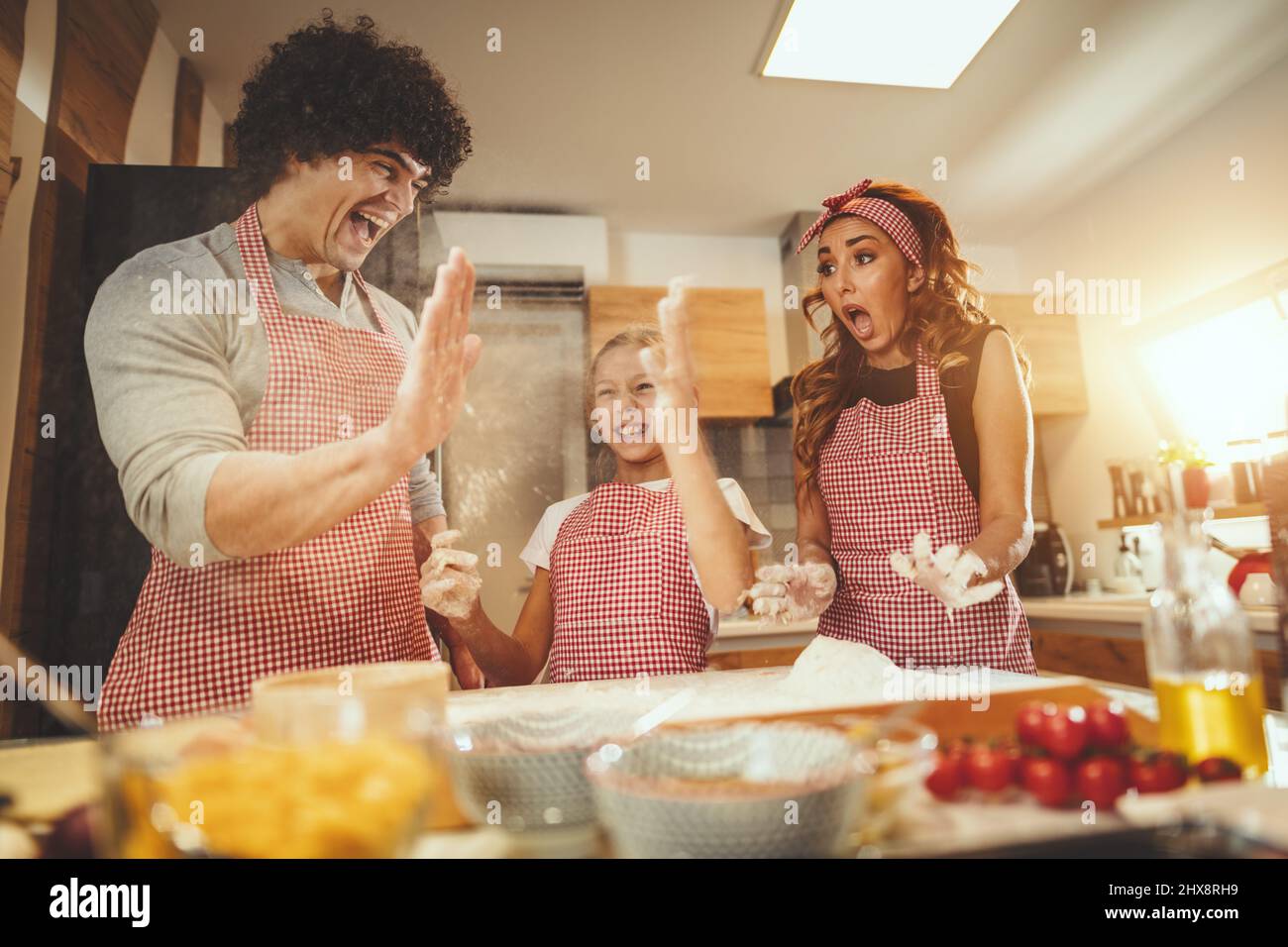 Happy parents and their daughter are having fun and preparing dough for pizza together in the kitchen. Little girl helps to her parents to mix dough o Stock Photo