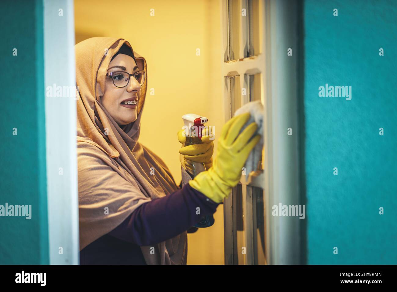 Middle aged Muslim businesswoman wearing hijab is standing by the window looking outside and washes window windows. Stock Photo