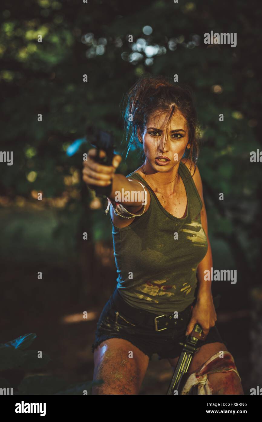 Beautiful young woman holding gun and getting ready for the attack in abandoned ruin. Stock Photo