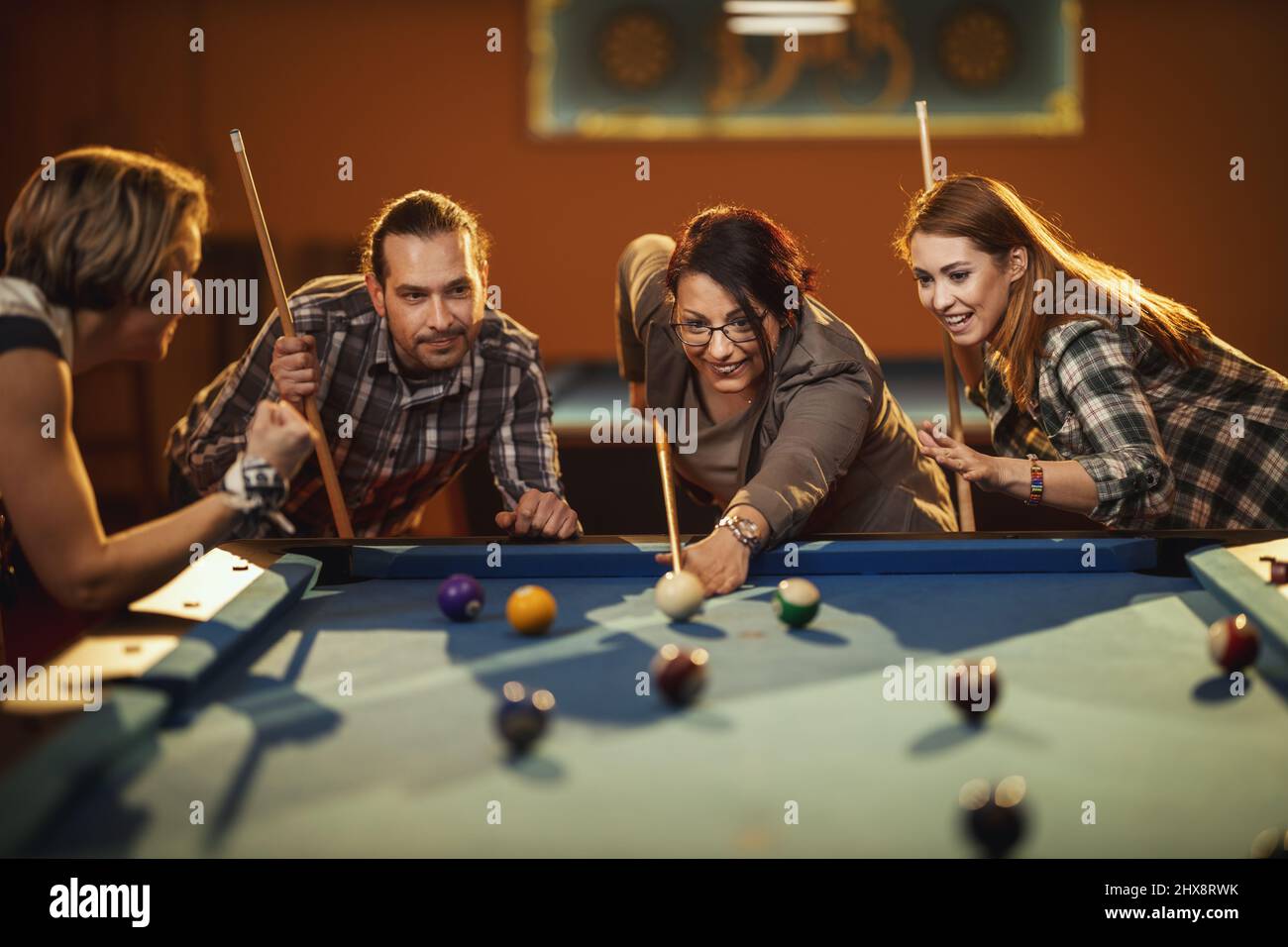 Young smiling cheerful friends are playing billiards in bar after work. They are involved in recreational activity. Stock Photo