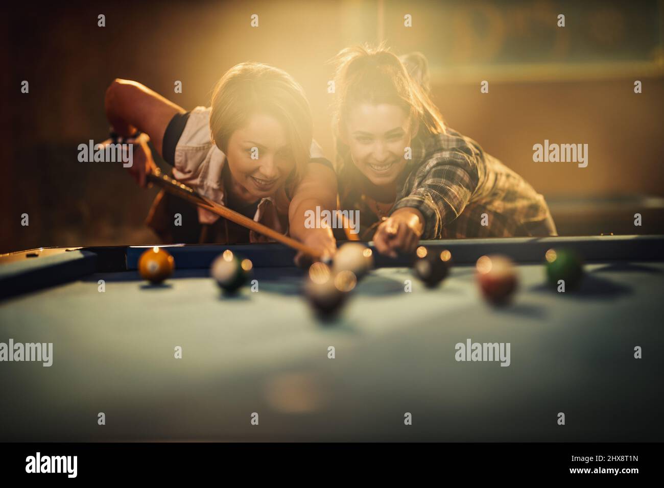 Young smiling cheerful two young women are playing billiards in bar after work. They are involved in recreational activity. Stock Photo