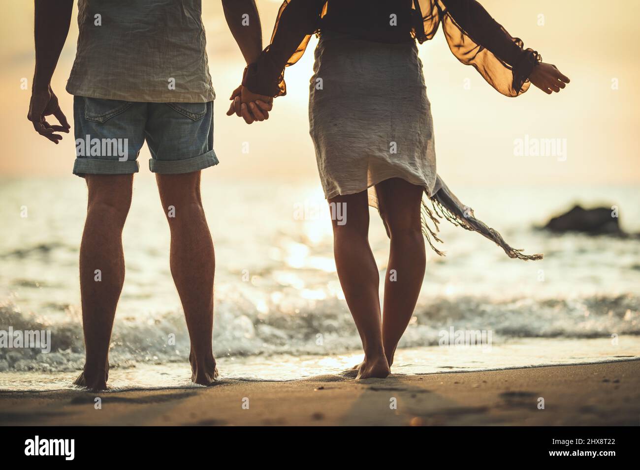 Close-up of a loving couple who is walking on the empty sandy sea beach at the sunset. Stock Photo