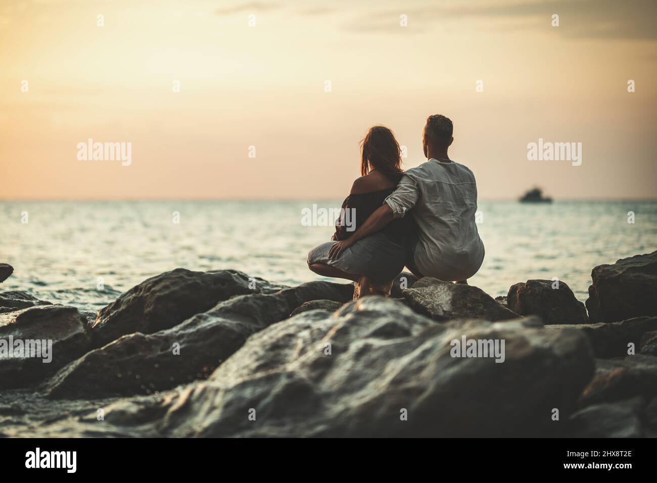 A loving couple is having fun and hugging on the empty sandy sea beach at sunset.They are looking away. Stock Photo