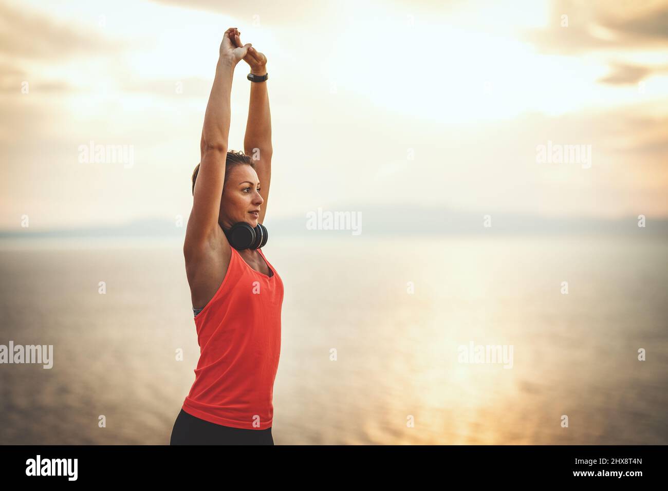 A beautiful young woman is doing stretching exercise at the sea beach in sunrise. Stock Photo