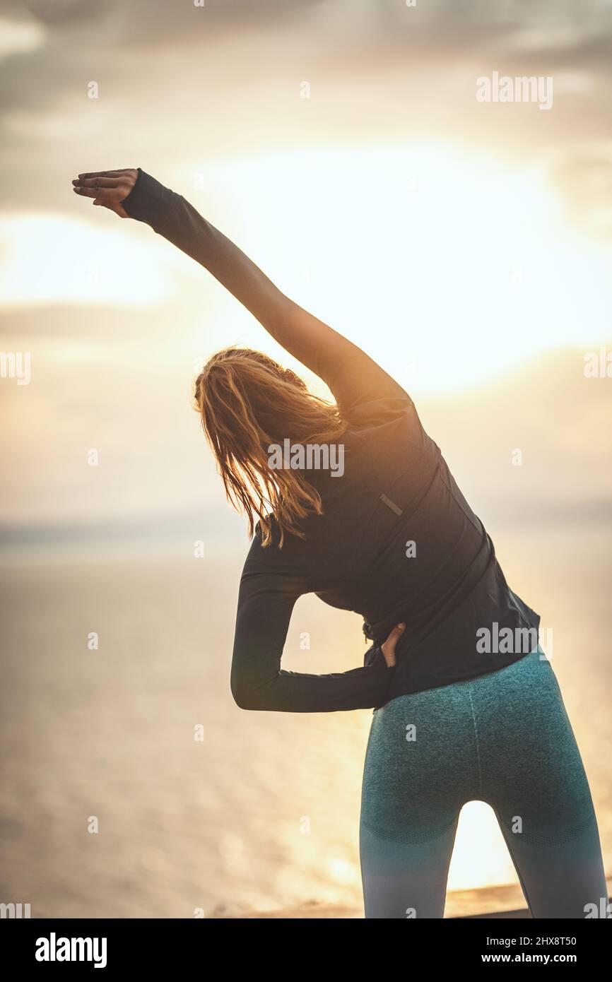 A beautiful young woman is doing stretching exercise by the ses in sunrise. Stock Photo