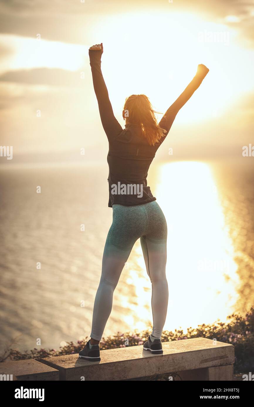A beautiful young woman is doing stretching exercise at the sea beach in sunset. Stock Photo