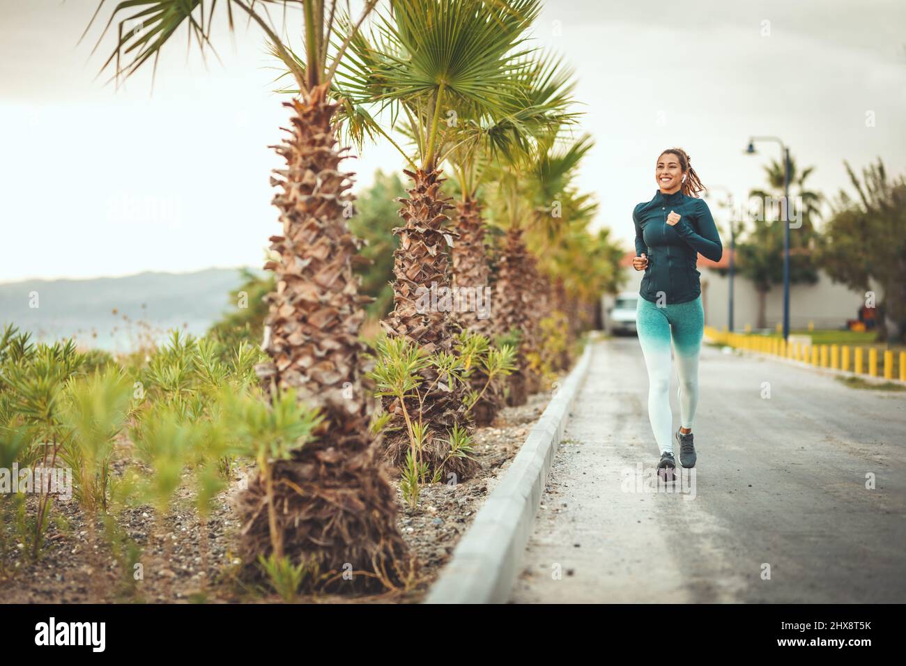 A beautiful woman is running along the path of a Mediterranean town by the sea and enjoying in summer sunny day. Stock Photo