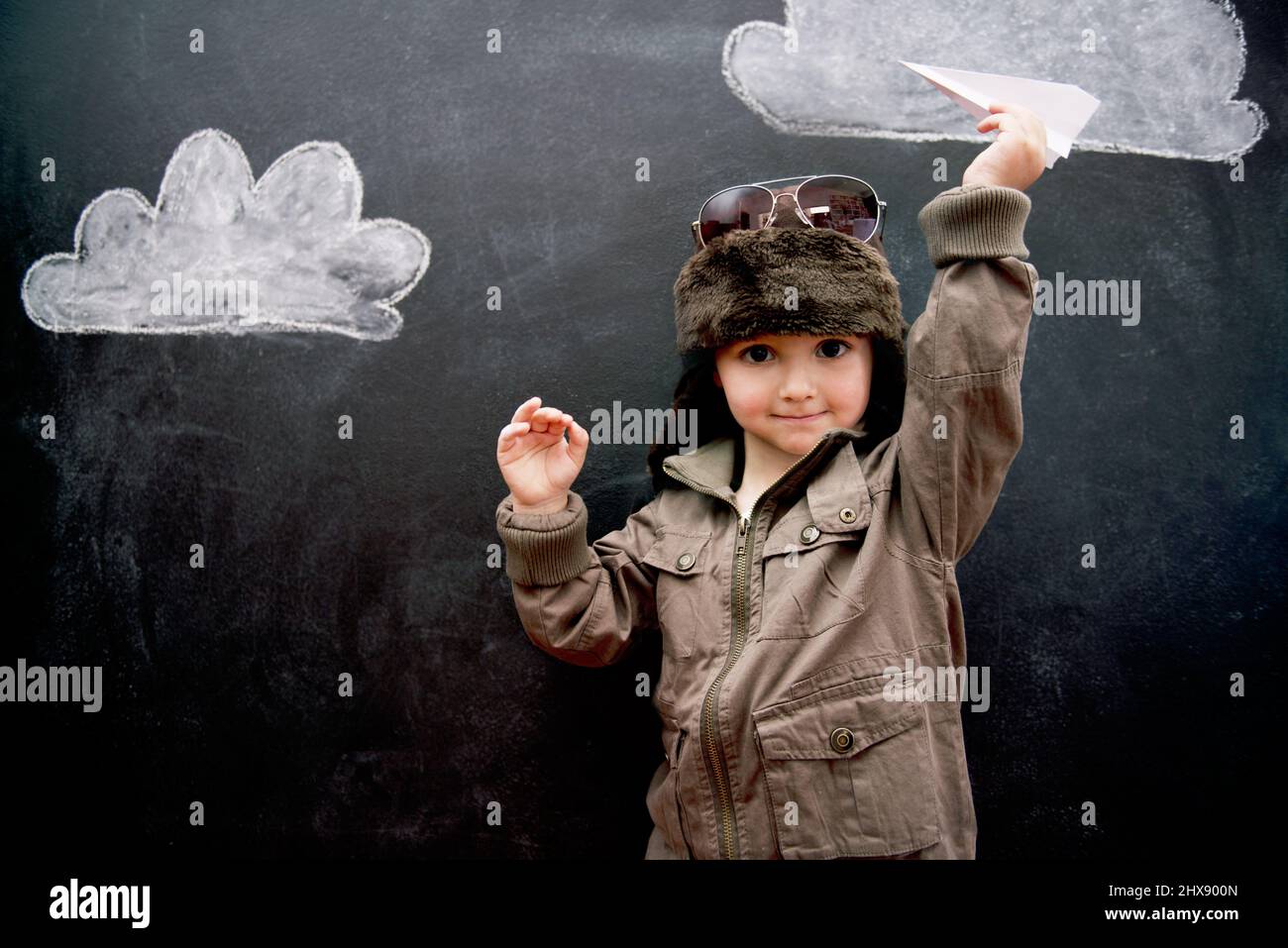 With education, anything is possible. A little boy playing with an airplane in front of clouds drawn on a blackboard. Stock Photo