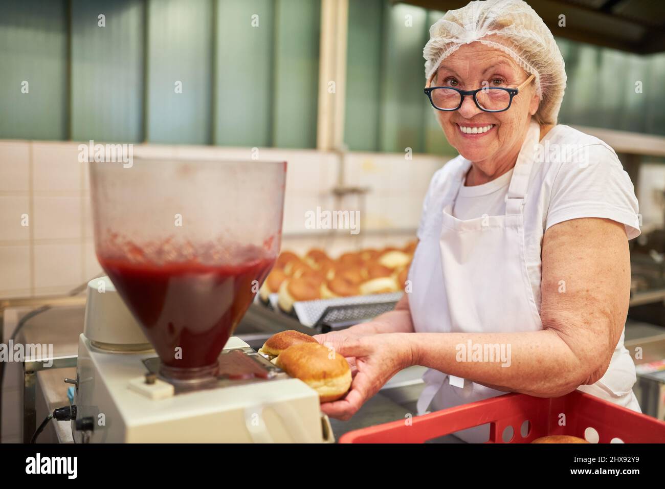 Woman as a baker when filling Berlin pancakes with jam in the bakery