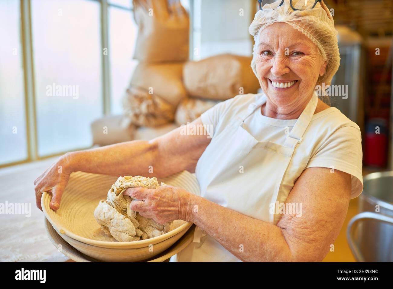 Happy elderly woman baker kneading dough in a bowl in preparation for baking Stock Photo