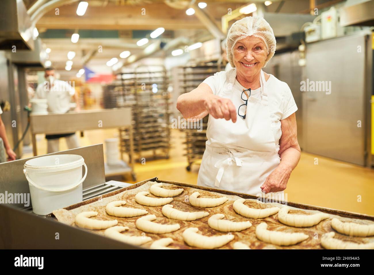 Elderly woman as an experienced baker sprinkles croissants with poppy