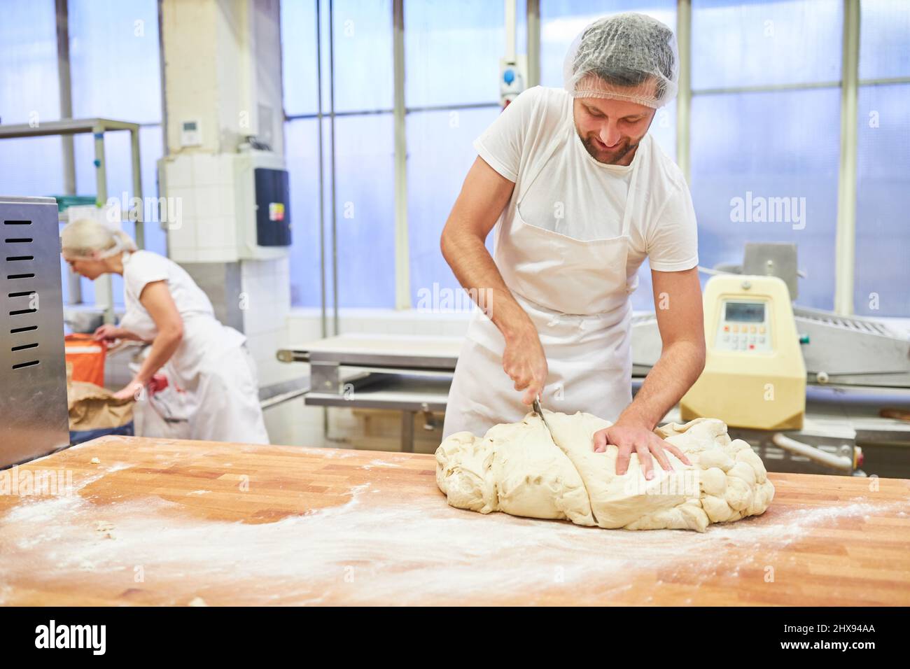 Young man as a baker cutting the dough in preparation for baking bread in the bakery Stock Photo
