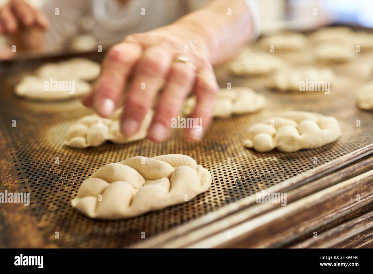 Baker's hand baking yeast plaited bread on a tray in the bakery Stock Photo