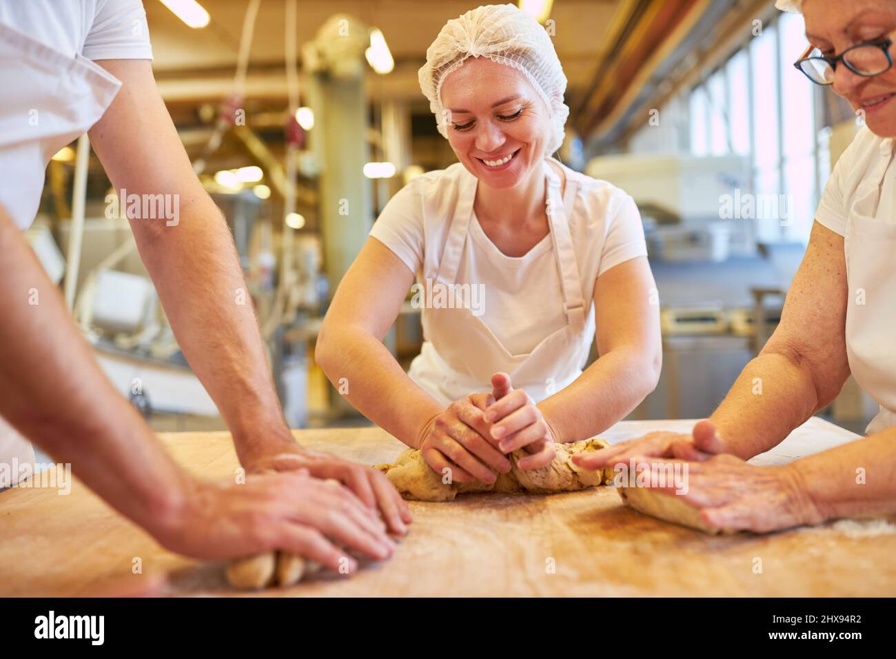 Young woman as a trainee baker kneading dough under supervision in a