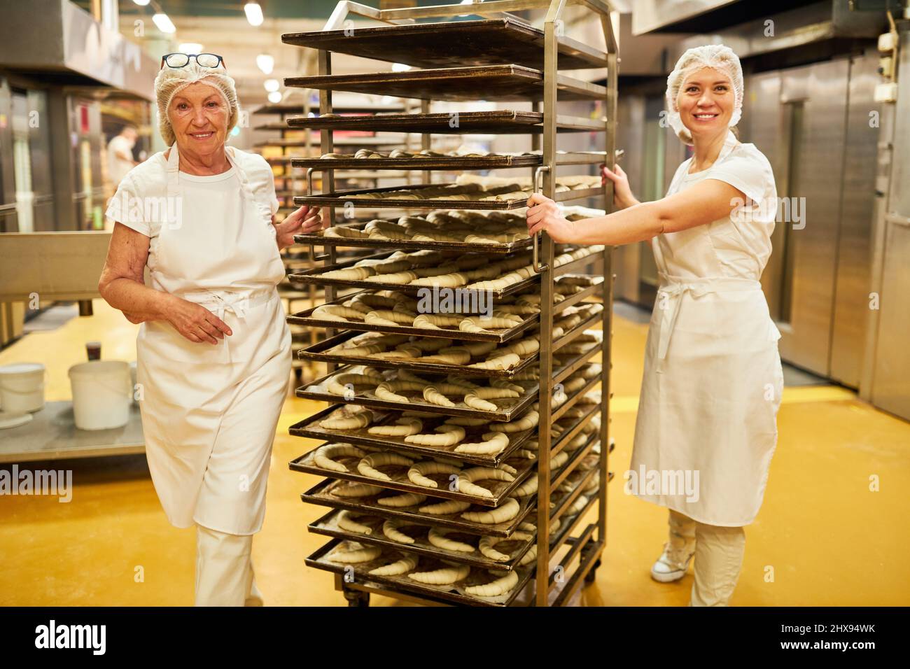 Two bakers push shelf trolleys with croissants for baking in the bakery