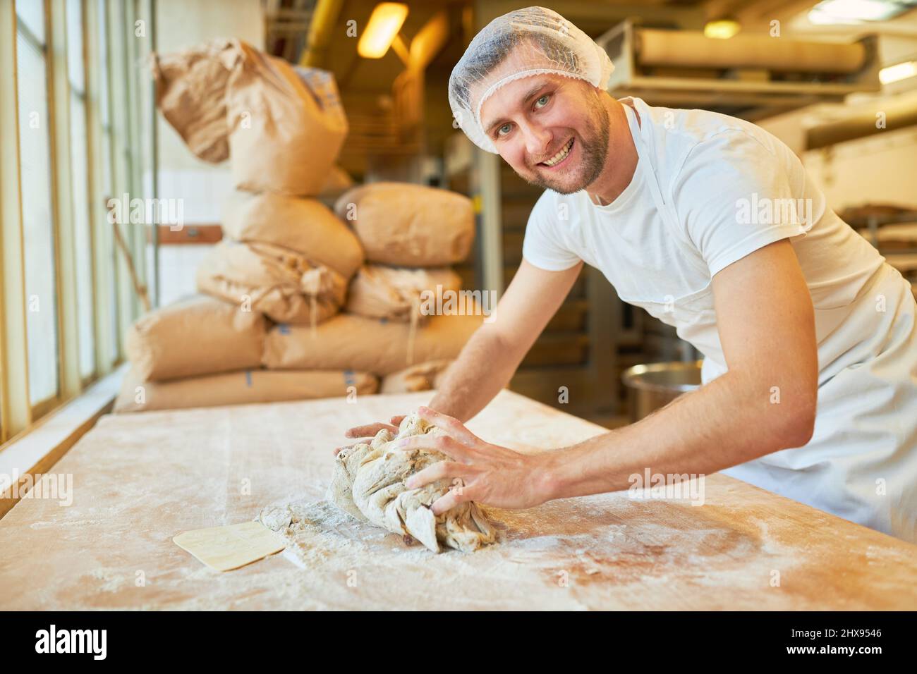 Young baker kneads dough as work step and preparation for baking bread in bakery Stock Photo