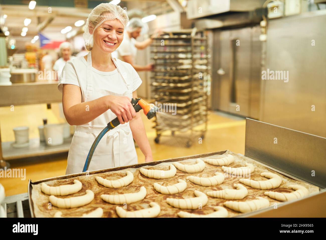 Young woman as a baker's apprentice moistens croissants with water in preparation for baking Stock Photo