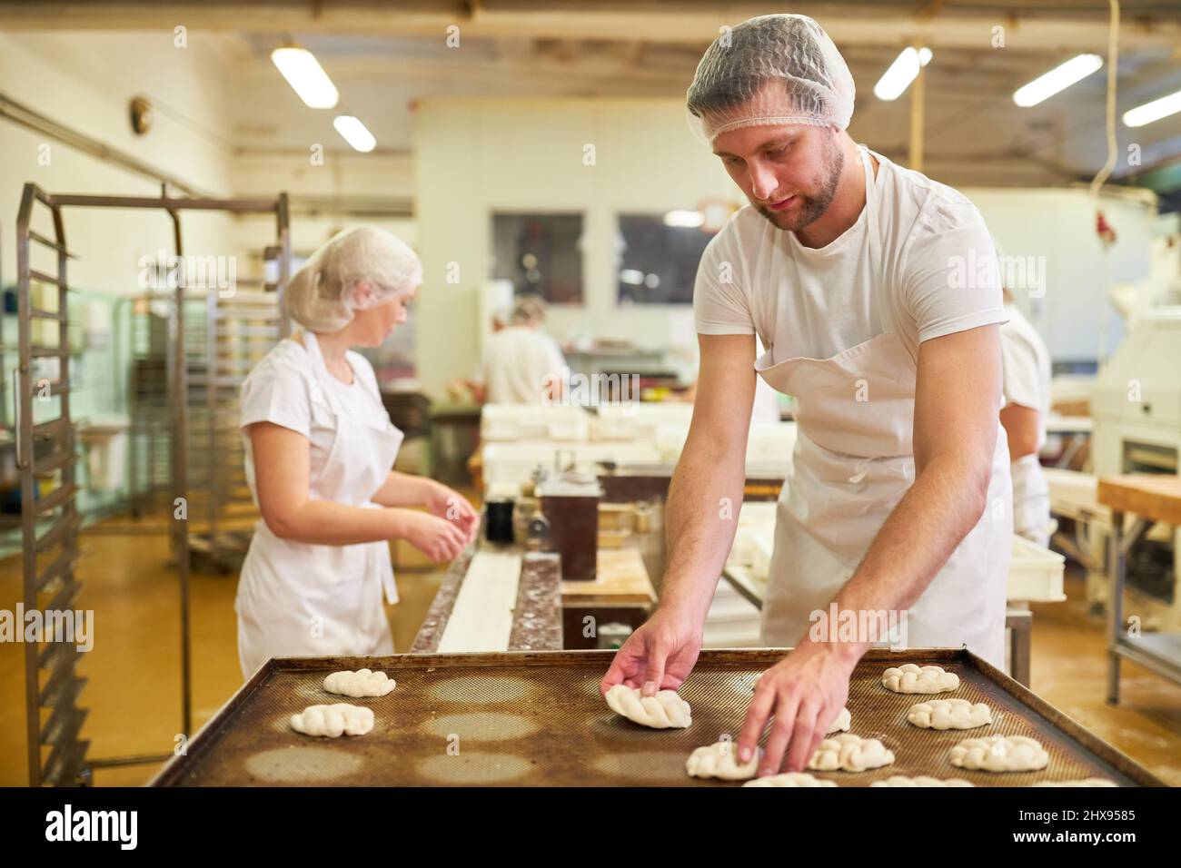 Young man as an apprentice in training to a baker on a baking tray with yeast plaits in a