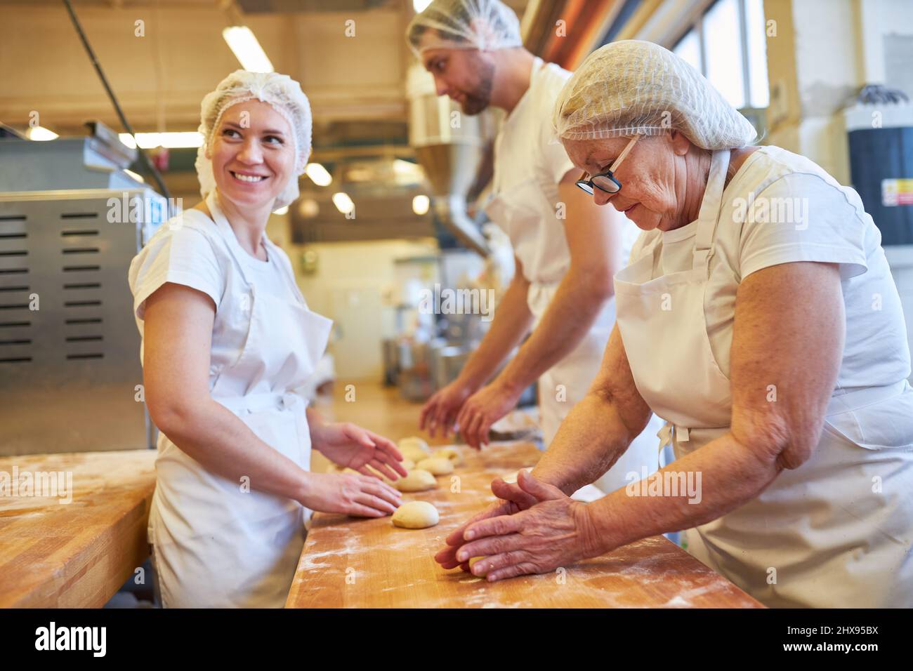 Young woman as a baker's apprentice kneading dough under supervision in