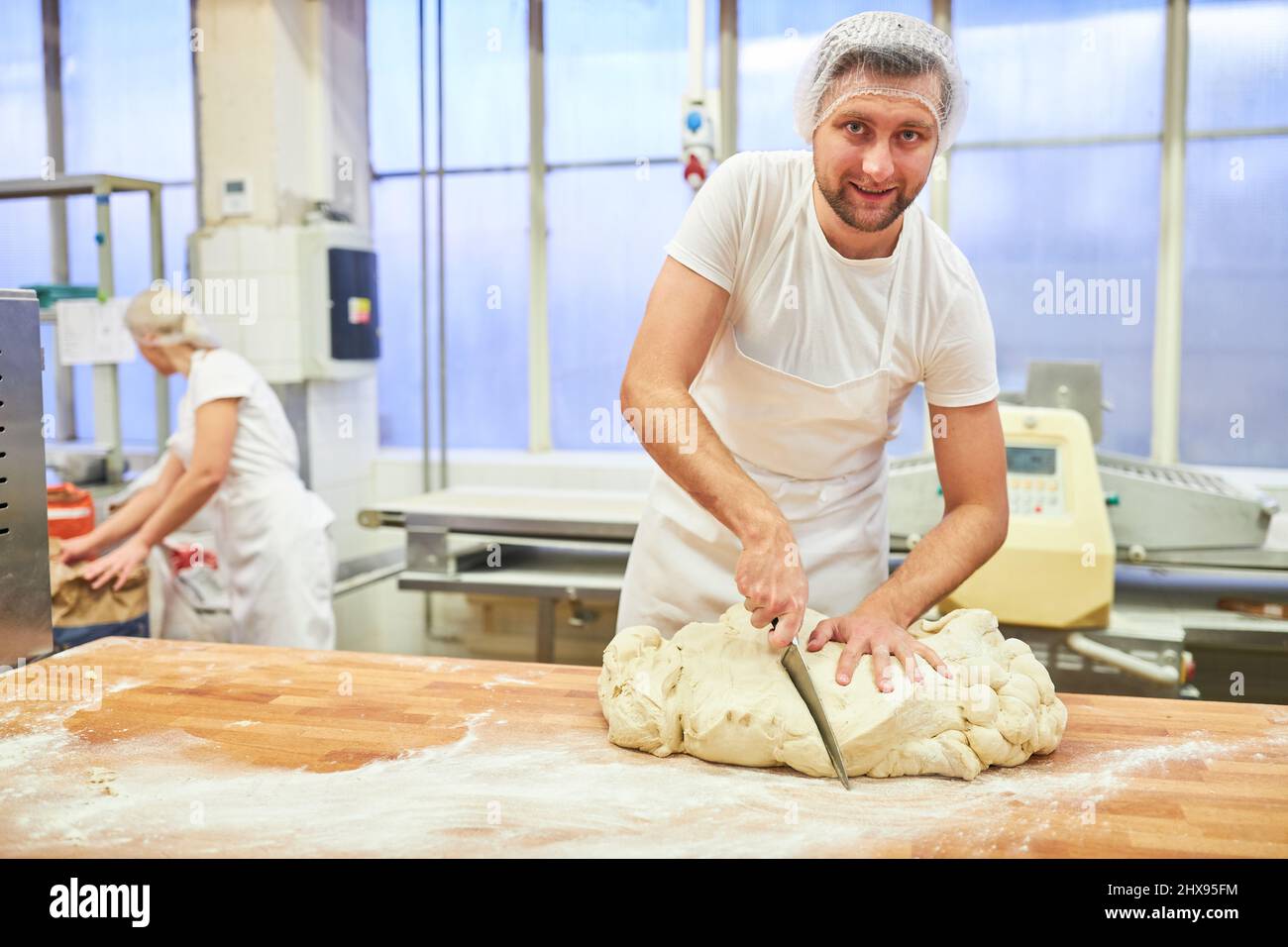 Baker trainee cuts dough with a knife while kneading bread dough Stock Photo