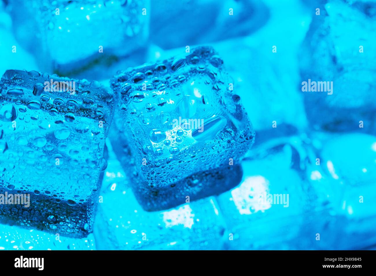 Ice made of cubes lined up with drops on a blue background Stock Photo