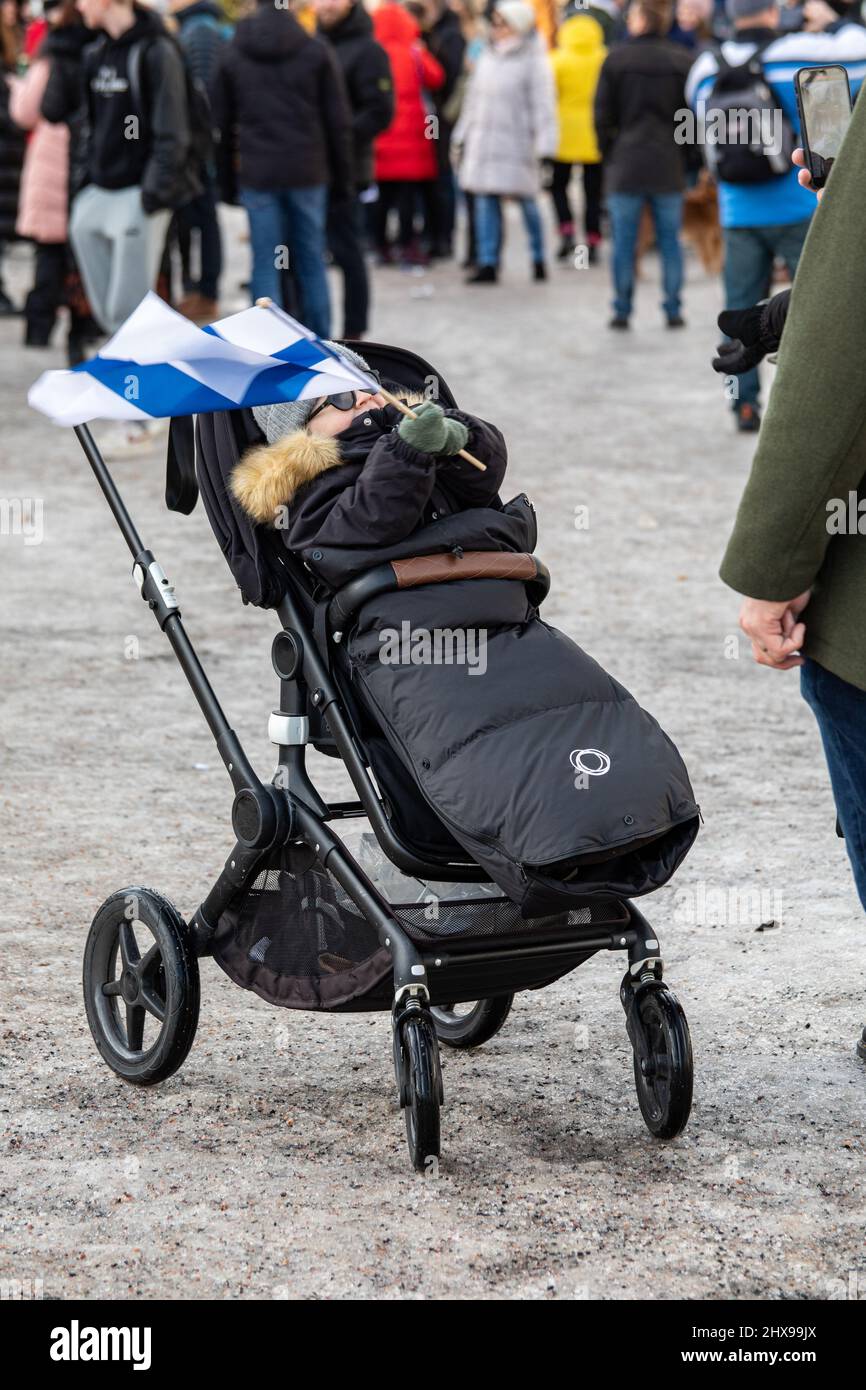 Child in a stroller or a pushchair waving miniature flag of Finland in celebration of Finnish ice hockey team's Olympic gold. Helsinki, Finland. Stock Photo