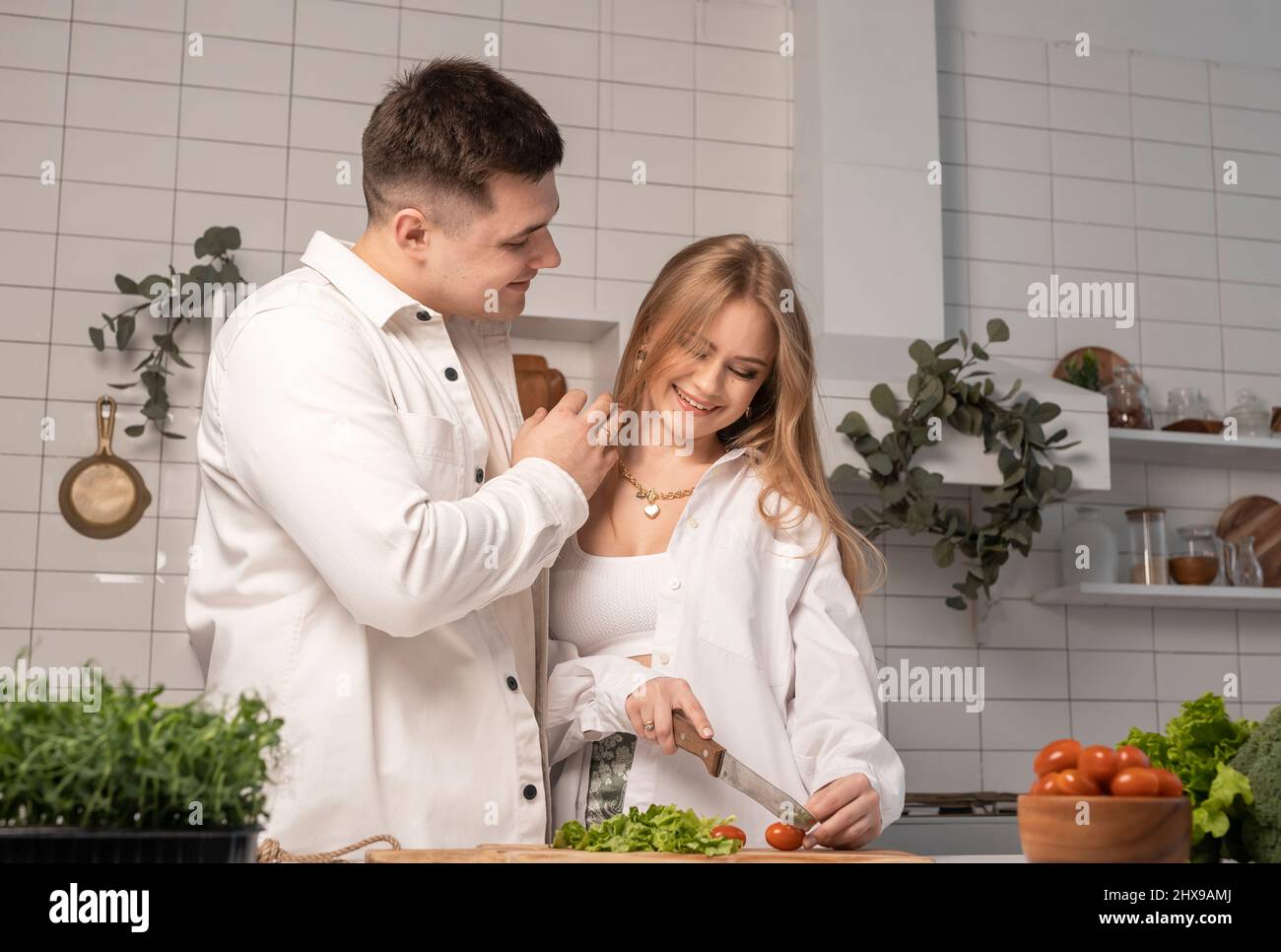 Happy couple cooking talking laughing at home. Handsome man embracing his wife or girlfriend while woman making vegetables salad. Healthy lifestyle concept. High quality photo Stock Photo