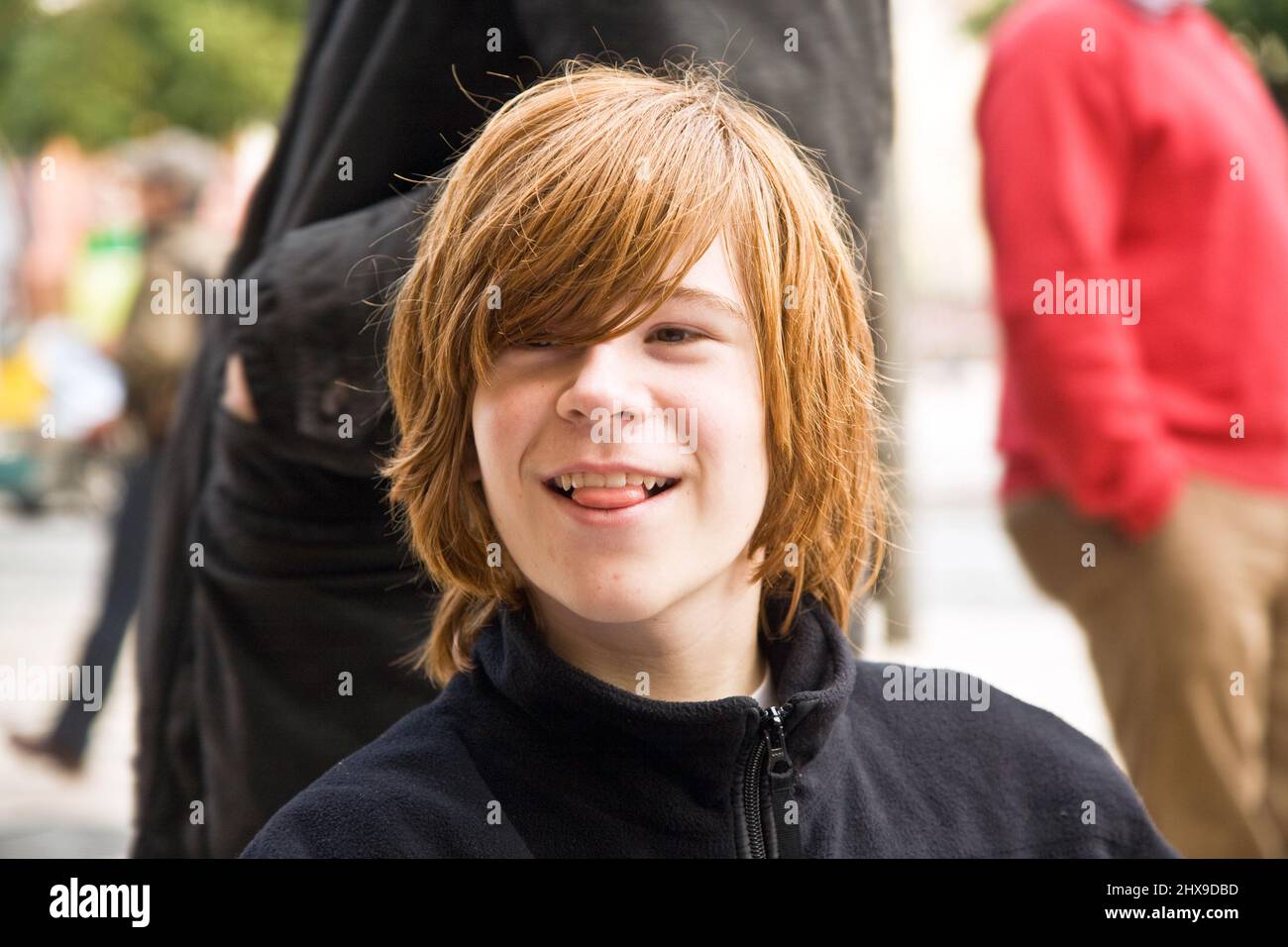 boy with long red hair pokes his tongue as a joke  and smiles Stock Photo