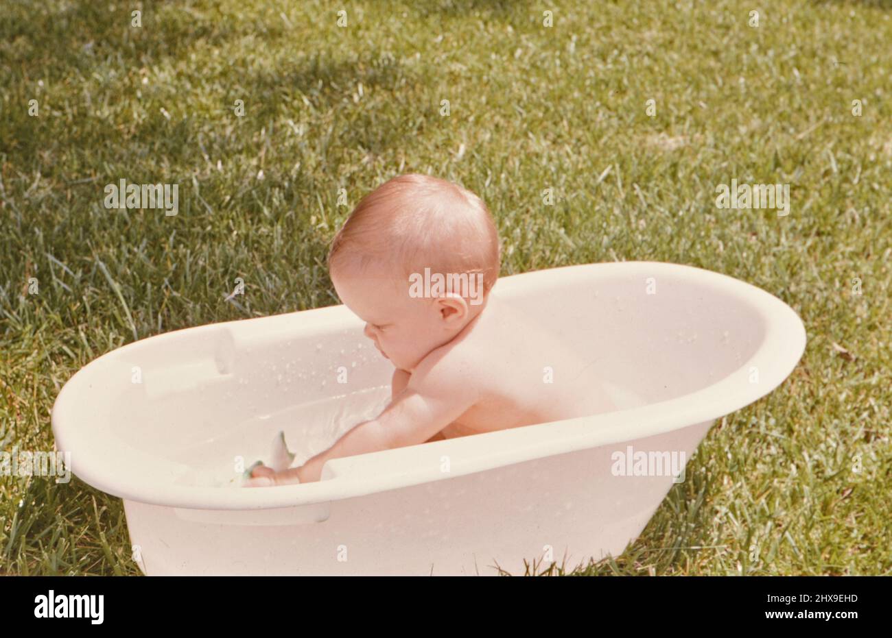 Twelve month old baby girl sitting outside in a bathtub ca. 1964 Stock