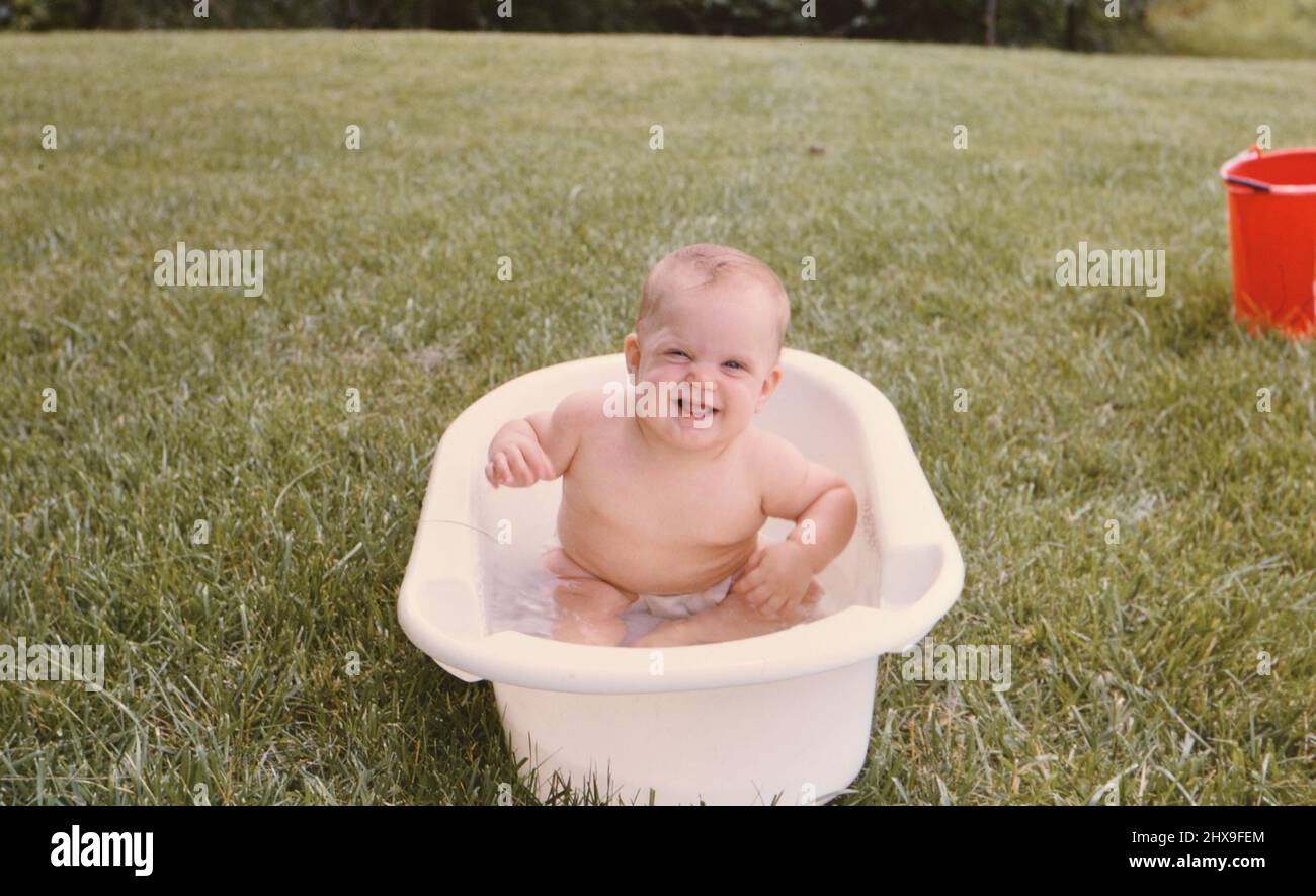 Happy 12 month old baby girl having fun in a bathtub in her yard ca