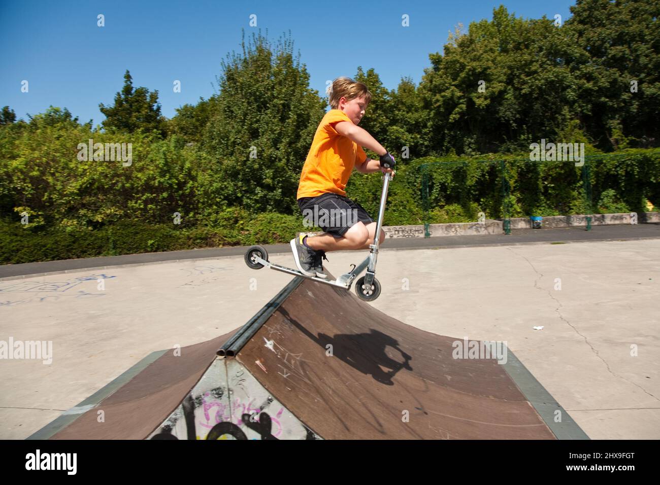 boy is jumping with a scooter over a spine in the skate parc and ...