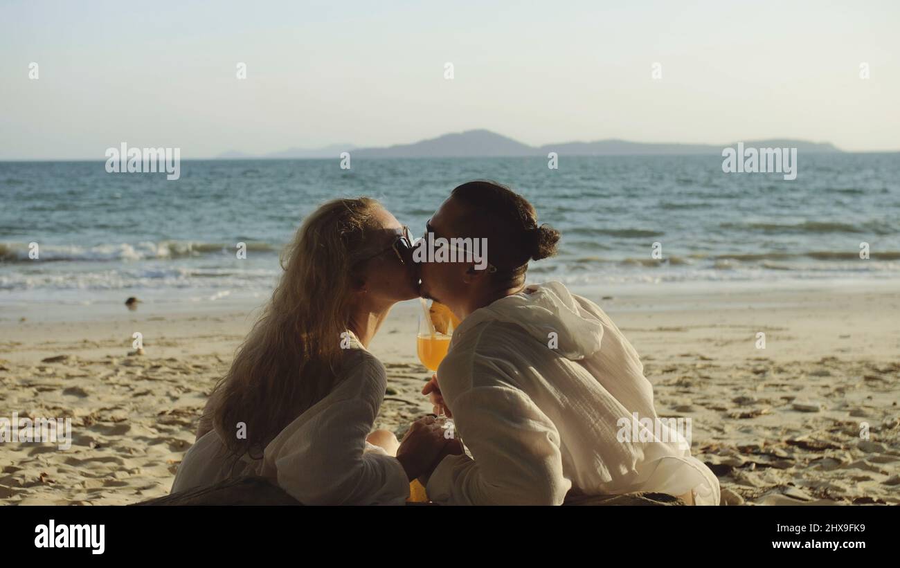 Loving couple in white dress, sunglasses, kissing, relax and drinking cocktail Pina Colada, pineapple slice. Concept sea beach resting tropical touris Stock Photo