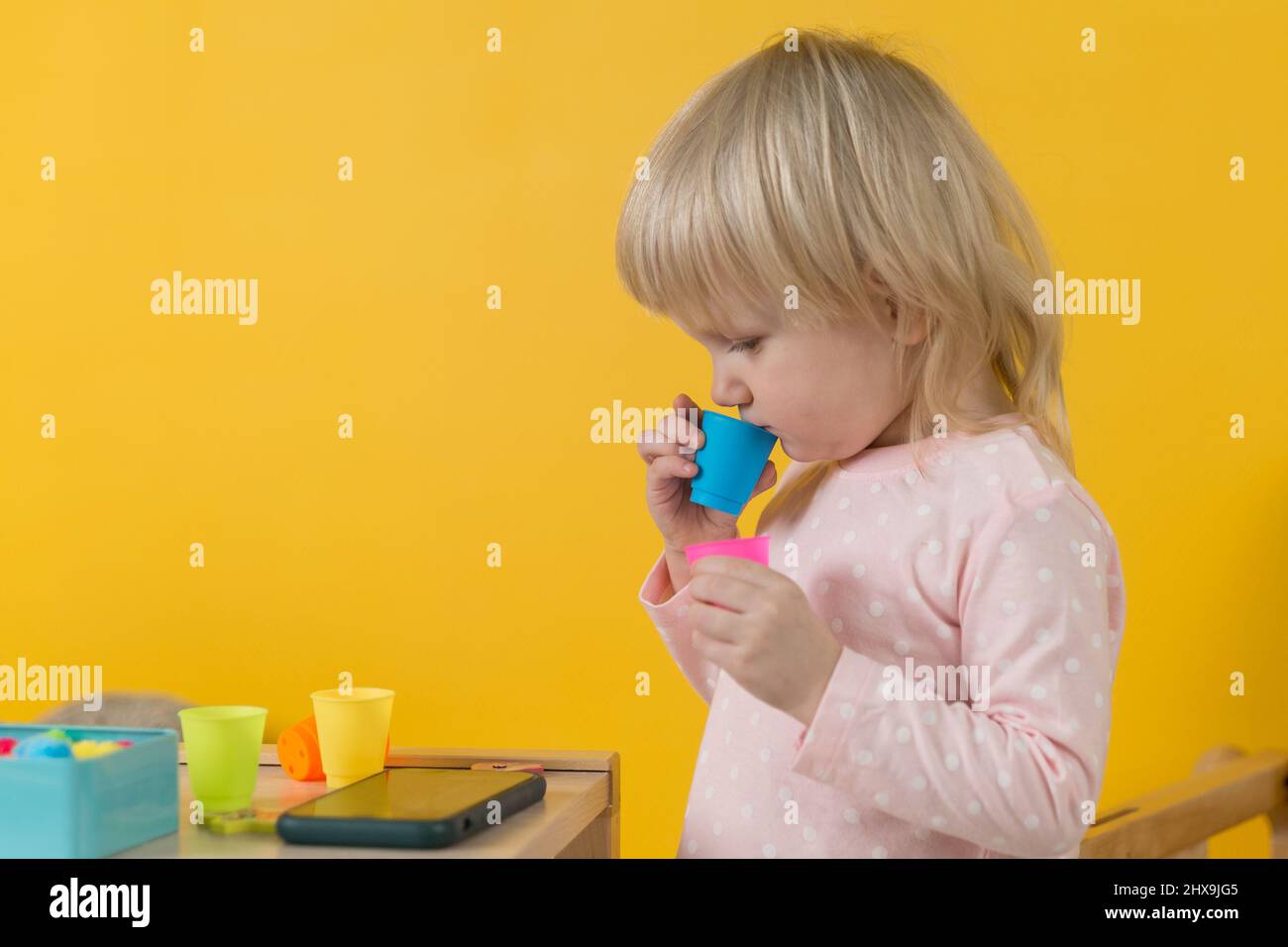 A girl in pink pajamas against a yellow wall enthusiastically