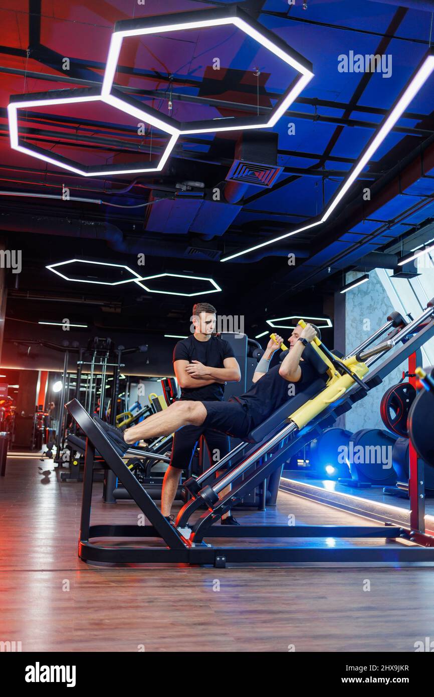 Athletic man doing exercises with the help of his personal trainer in a ...