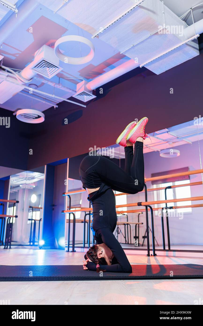 Young beautiful plastic woman in black suit standing on her head on the floor and working hard
