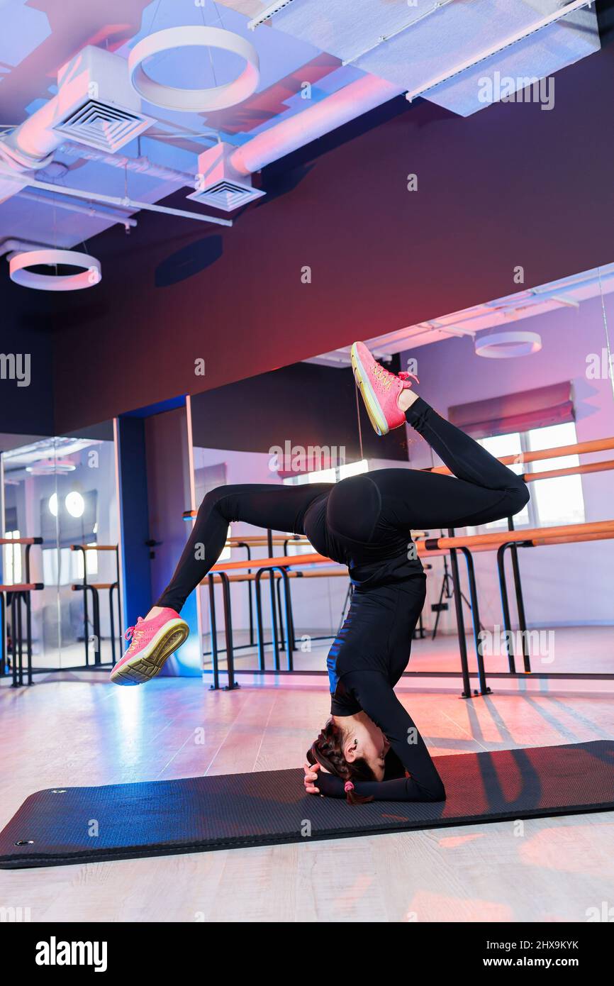 Young beautiful plastic woman in black suit standing on her head on the floor and working hard