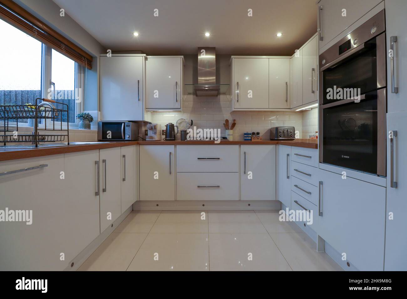 Ultra modern white kitchen with wooden worktop and shiny tiled floor