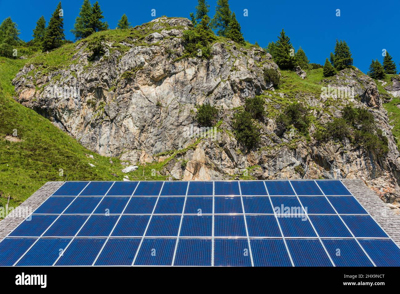 Solar photovoltaic panels against the backdrop of rocky mountains covered with green plants and trees Stock Photo