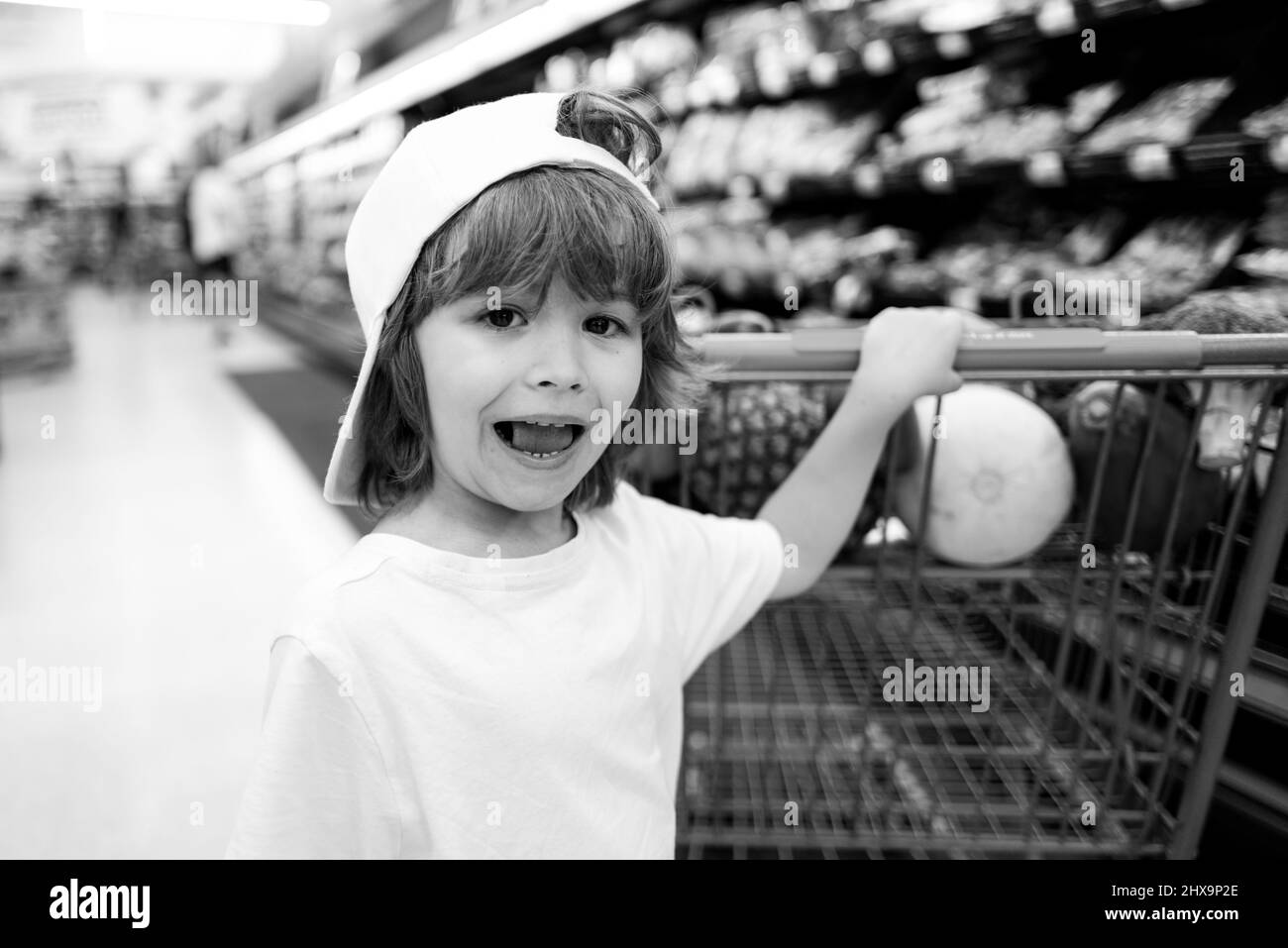 Customer child holdind trolley, shopping at supermarket, grocery store. Little boy in the supermarket. Cute boy child with shopping trolley with Stock Photo